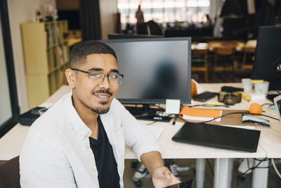 Portrait of confident computer hacker sitting at desk in office