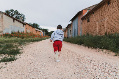 Back view of a unrecognizable boy running outdoors in an old town on a cloudy day