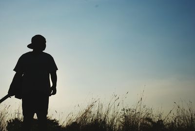 Rear view of silhouette boy standing on field against clear sky
