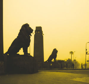 Statue of man with dog against sky during sunset