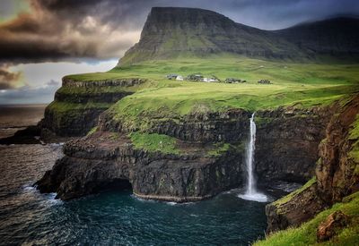Scenic view of waterfall and sea by mountains against cloudy sky