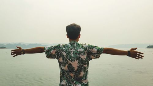 Rear view of man standing by sea against clear sky