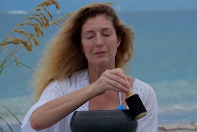 Woman meditating with singing bowl with wooden striker at beach