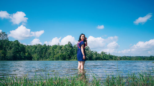 Young woman standing by lake against sky