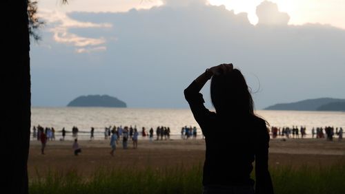 Silhouette woman looking people at beach against sky
