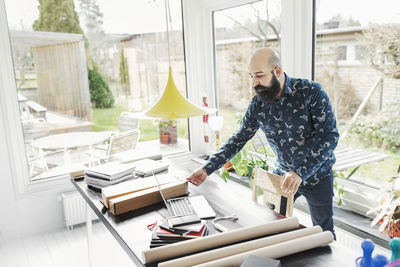 Male architect working at table in home office by window