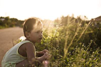 Side view of boy crouching by plants during sunset