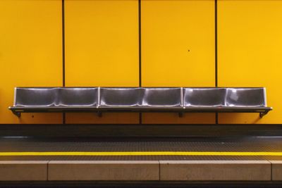 Metal seat on yellow wall in subway railroad platform