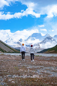 Rear view of men standing on snowcapped mountain against sky