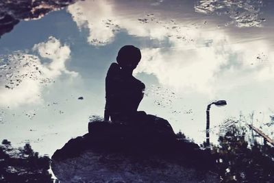 Low angle view of woman standing on rock against cloudy sky