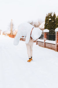 Rear view of man carrying stuffed toy while walking on snow