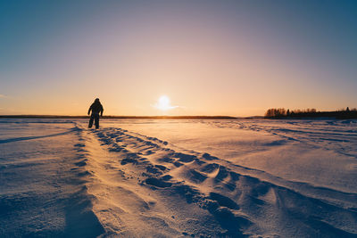 Silhouette person on snowy land against sky during sunset