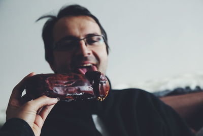 Cropped hand feeding sweet food to male friend against wall