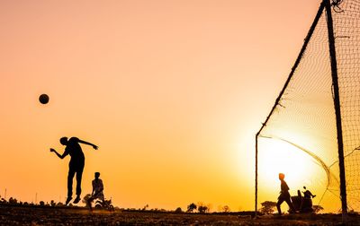 Silhouette people playing with ball against sky during sunset