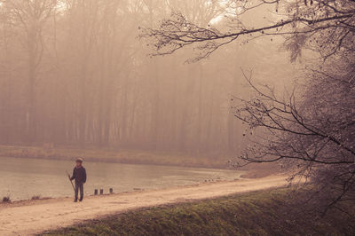 Full length of boy walking by lake during foggy weather