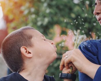 Son blowing dandelion held by mother outdoors