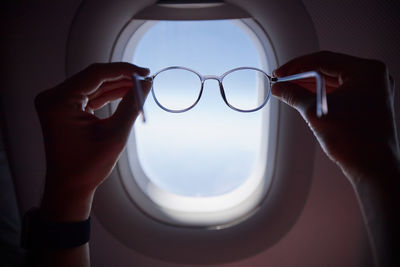 Hand of passenger holding eyeglasses against airplane window during flight. 