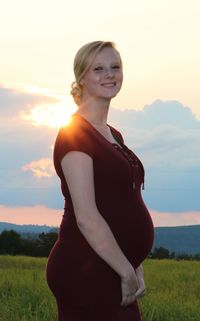 Portrait of pregnant woman standing on field against sky during sunset