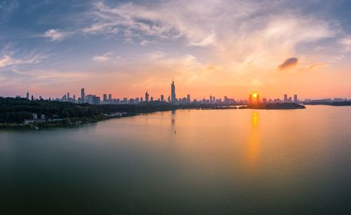 Scenic view of river by buildings against sky during sunset