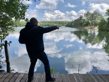 Rear view of man standing by lake against sky