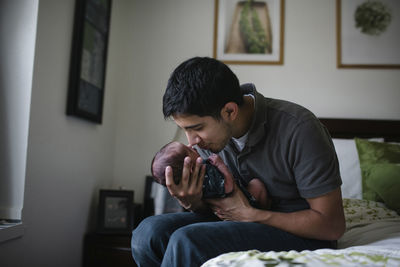 Father playing with newborn son while sitting on bed at home