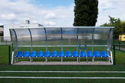 Crutches or medicine sticks  at blue plastic seats on outdoor football players bench below roof