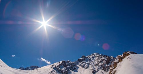 Low angle view of snowcapped mountains against blue sky