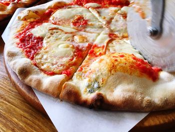 Close-up of cutter cutting pizza served on table