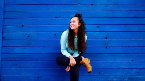 Smiling young woman standing against blue wooden wall