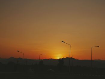 Silhouette street lights against sky during sunset