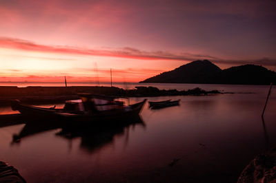 Sailboats moored on sea against orange sky