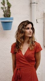 Beautiful young woman looking away while standing against wall