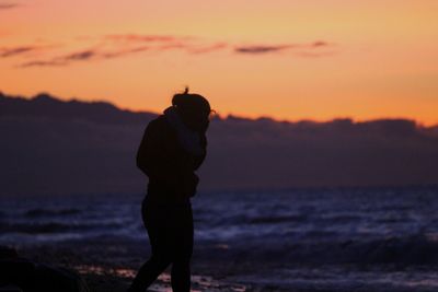 Silhouette man standing on beach against sky during sunset