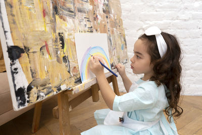 Cute girl drawing rainbow on white sheet on a drawing easel. little painting artist.
