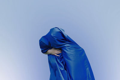 Girl covered with blue fabric against colored background
