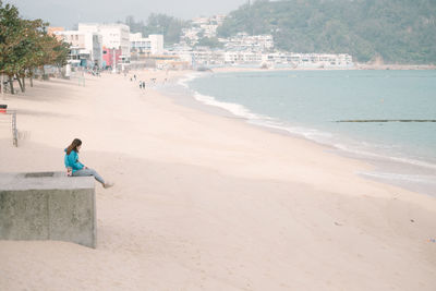 Woman sitting on retaining wall at beach