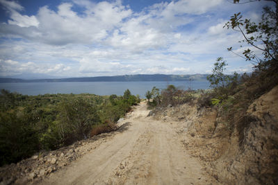 Dirt road by sea against sky