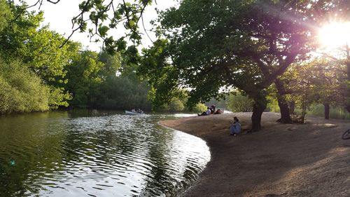 People on river amidst trees against sky