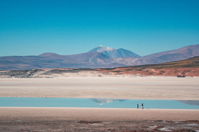 Scenic view of lake by mountains against clear blue sky