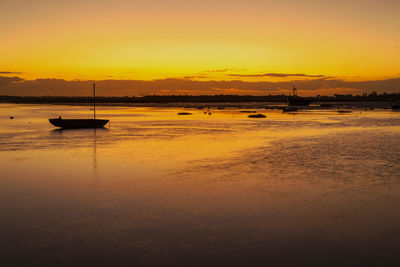 Boats moored on sea against orange sky