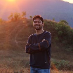 Portrait of smiling young man standing on land at sunset