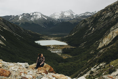 Full length of woman sitting on rock at mountain peak