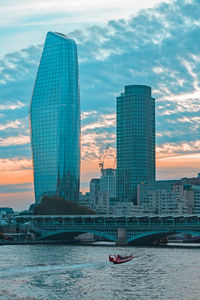 Bridge over river by buildings against sky during sunset