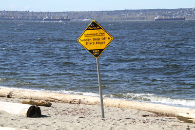Yellow and black sign indicating submerged pipe and drop off on post in the middle of a sandy beach