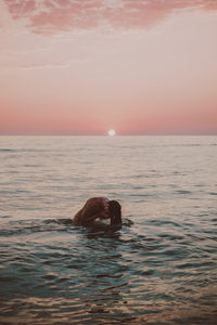 Woman swimming in sea against sky during sunset