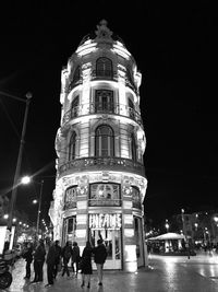 People walking on illuminated street amidst buildings in city at night