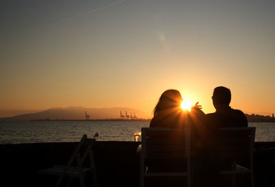 Silhouette couple sitting by sea against sky during sunset