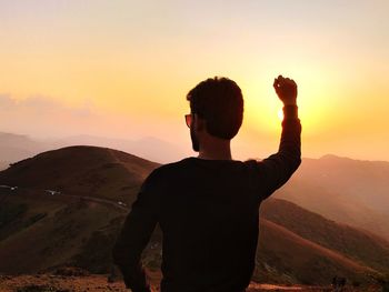 Rear view of man standing on mountain at sunset