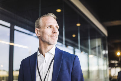 Smiling male entrepreneur looking away while standing in office corridor