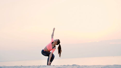 Healthy, young beautiful woman meditating, practicing yoga on the sea beach, at sunrise, makes